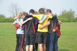 Gruppe an Jugendlichen bildet einen Mannschaftskreis auf einem Sportfeld.